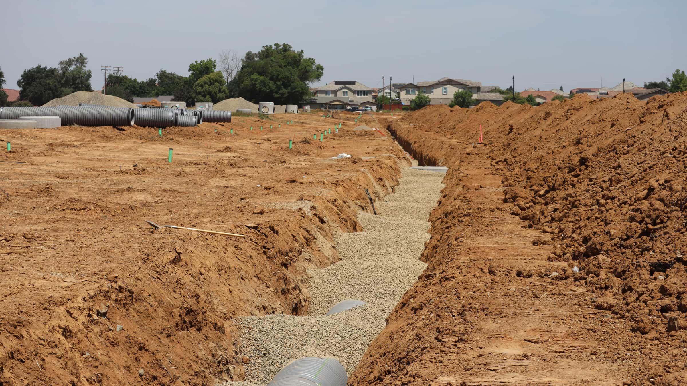 An open trench excavation on a residential property with compaction equipment during underground utility installation.